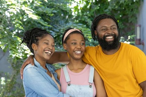 African american family laughing and smiling in sunlit backyard embracing teen daughter