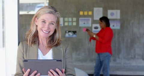 Mature businesswoman using tablet with team collaborating in modern office