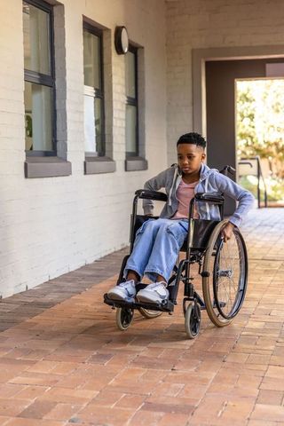 African american boy pushing manual wheelchair on brick path demonstrating mobility