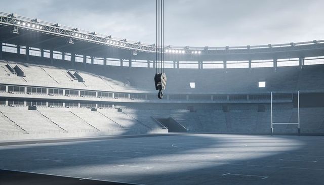 Heavy-duty crane hook suspended over empty stadium bowl highlighting concrete tiers