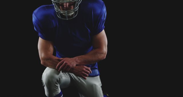This image shows an American football player kneeling with a solemn expression, dressed in a full football uniform and helmet. The motionless pose suggests themes of contemplation, preparation, or respect. Ideal for use in articles or advertisements relating to sports, athleticism, determination, and team spirit. Suitable for promoting fitness programs, sports equipment, mental focus in sports, and motivational content.