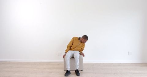 Young Man in Casual Hoodie Sitting Thoughtfully in Minimalist Room