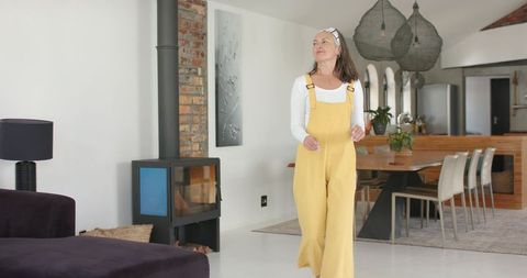 Woman strolling through modern minimalist open-plan living area wearing mustard yellow overalls