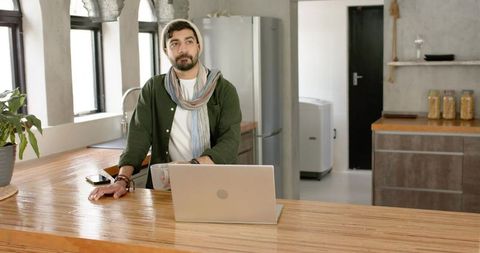 Indian man working from kitchen island with laptop and coffee, remote work lifestyle