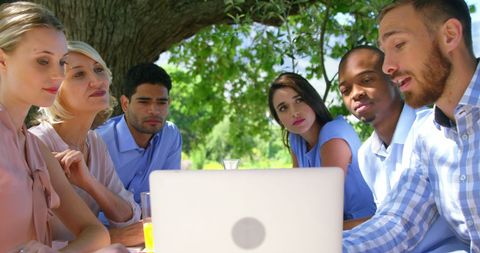 Diverse Group Sharing Ideas Outdoors Around Laptop