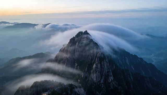 Jagged granite peak cascading clouds at sunrise over misty mountain ridgelines and sweeping valleys
