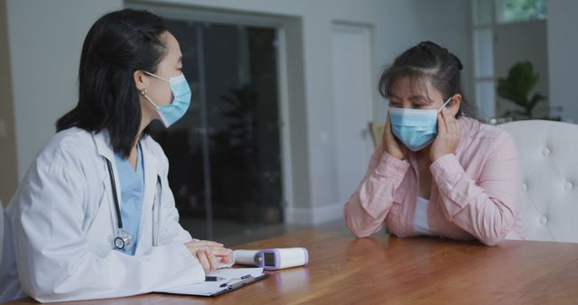 Asian female nurse wearing face mask in consultation with female patient wearing mask in hospital. medicine, health and healthcare services during coronavirus covid 19 pandemic.