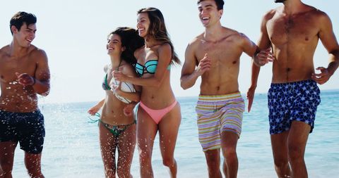 Carefree young adults laughing and splashing at sunny beach