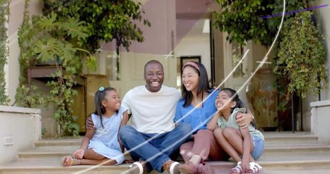 Joyful family sitting on front steps laughing together on sunny porch with potted plants