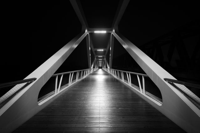 Depicts symmetry and interesting perspective of a modern bridge at night highlighted by dramatic lighting. Ideal for use in architectural portfolios, urban environment presentations, design-focused advertising, and illustrating concepts of modernity and structure.