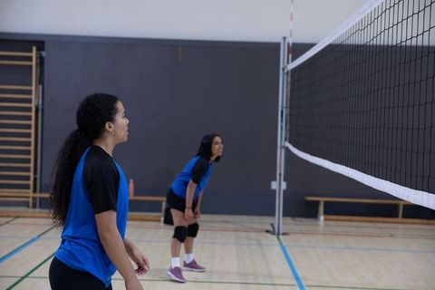Diverse female volleyball players practicing defensive stance on indoor court with net
