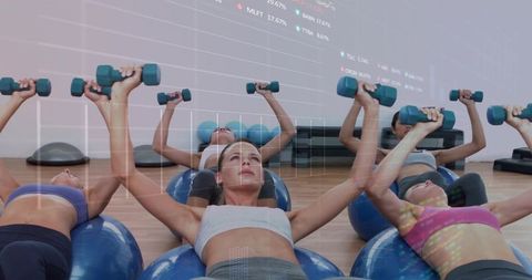 Women performing chest press on stability balls with dumbbells in group fitness class