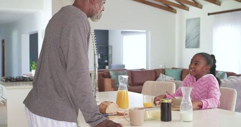 African american grandfather sharing breakfast with granddaughter at cozy kitchen island