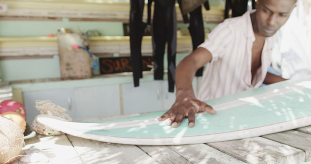 Man waxing surfboard in surf shop, prepping it for a surf session. Useful for articles and promotions related to surfing, beach activities, lifestyle, and adventurous sports.