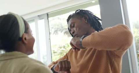 African American couple checking smartwatch and chatting in sunroom with garden view