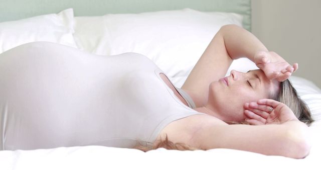 Pregnant woman relaxing on bed with hand on forehead - Download Free Stock Images Pikwizard.com