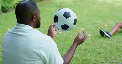 African american father catching soccer ball with son on backyard lawn, casual family play