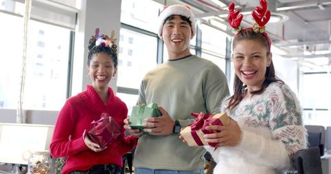 Multicultural coworkers exchanging holiday gifts in sunlit office celebrating team spirit