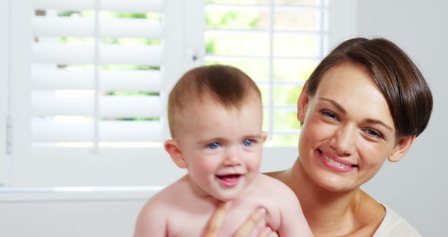 Smiling Mother Holding Happy Baby at Home Beneath White Shuttered Windows - Download Free Stock Images Pikwizard.com