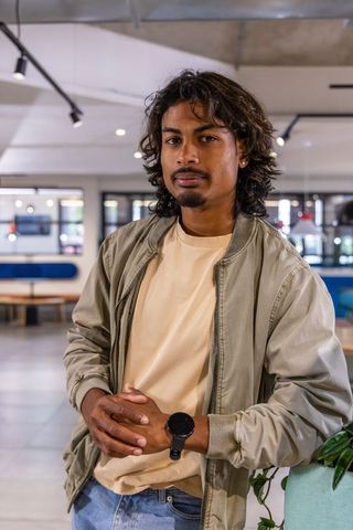 Young indian man leaning on planter in modern coworking space wearing bomber jacket