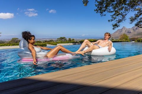 Diverse couple floating on pool floats relaxing by infinity pool with mountain view