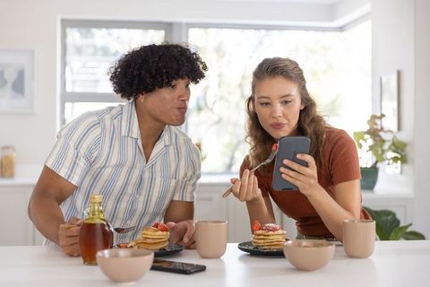 Young couple enjoying pancakes at sunlit kitchen counter sharing cozy morning together