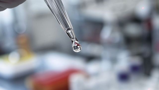 Close-up pipette droplet in laboratory with gloved hand and blurred scientific background