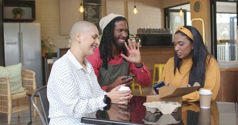 Multiracial Friends Sharing Laughter and Smartphones Over Takeaway Coffee in Modern Cafe