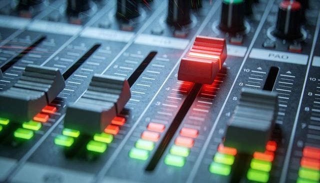 Red-lit fader riding on professional mixing console with glowing LED meters and tactile sliders