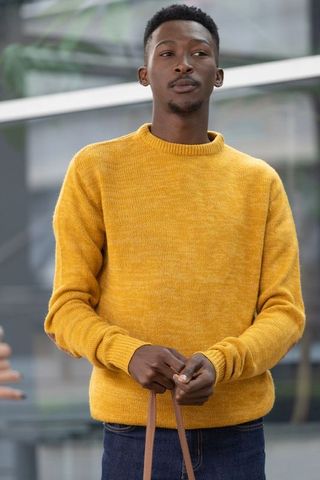 Contemplative african man wearing mustard sweater holding leather bag strap urban portrait