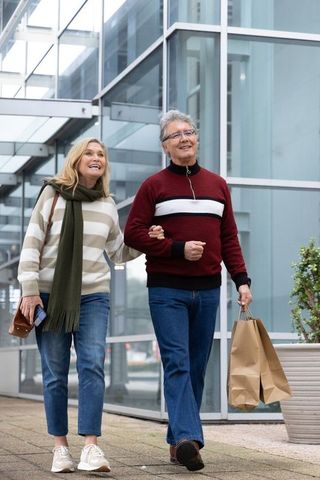 Senior couple walking arm-in-arm with shopping bags by modern glass facade