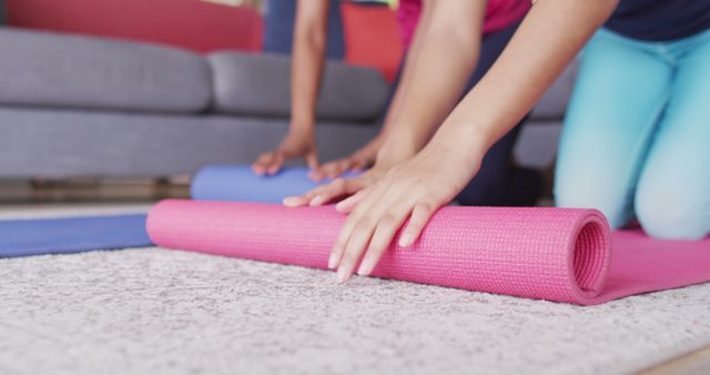 Women getting ready for a workout by rolling yoga mats. Indoor setting emphasizes home fitness. Perfect for promoting at-home exercise routines, healthy lifestyle, and fitness classes or products. Great for blogs, social media posts, and content related to wellness.