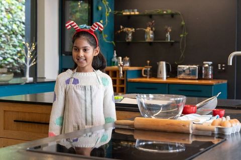 Indian girl wearing festive antler headband doing holiday baking at modern kitchen island