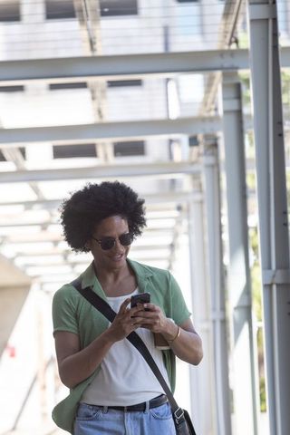 Male commuter walking along urban covered walkway checking smartphone wearing green shirt