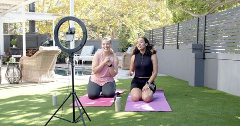 Diverse female friends filming yoga tutorial on sunny patio