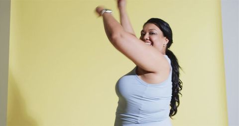 Energetic woman stretching arms on yellow background