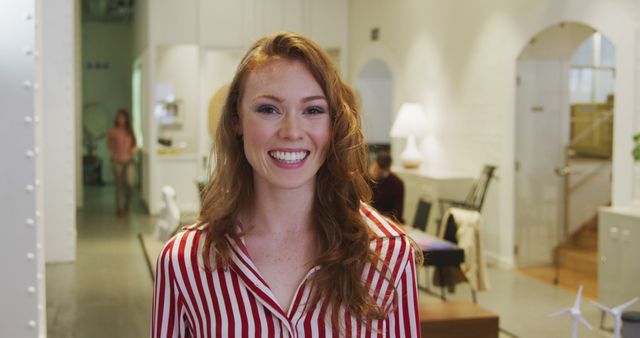 Portrait of a happy Caucasian businesswoman with long red hair working in a modern office, smiling to camera with her colleagues working in the background.