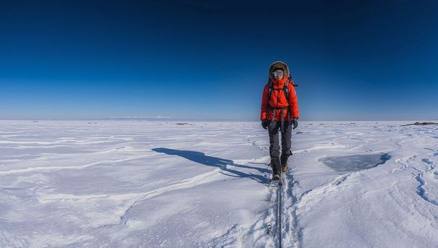 Solo polar explorer walking across vast frozen plain in red parka with safety rope