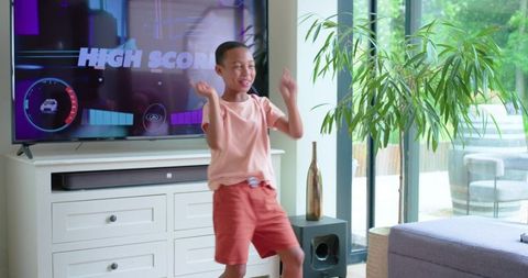 African american preteen boy celebrating high score while playing console game at home