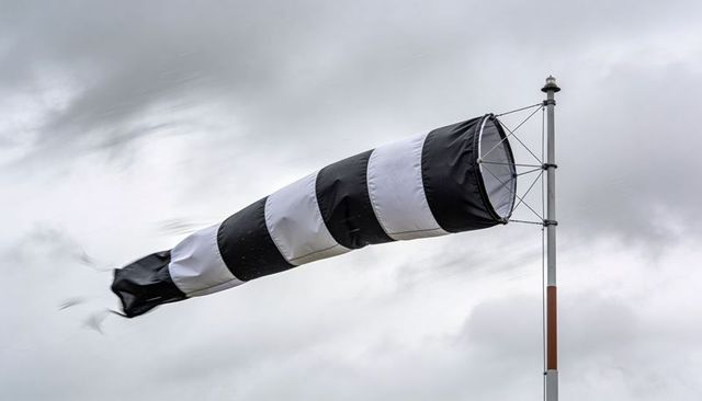Black-and-white striped windsock fluttering on pole against overcast sky for aviation use