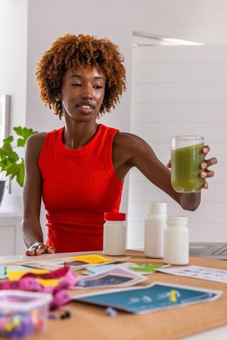 African american woman preparing green smoothie while organizing supplement jars and plans