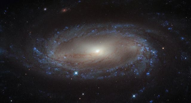 This beautiful image shows the spiral galaxy IC 2560, which lies more than 110 million light-years away from Earth in the Antlia constellation. IC 2560 is a Seyfert-2 galaxy characterized by its extremely bright nucleus and strong emission lines. This photograph captures its distinct spiral arms and barred structure, features emphasizing the beauty and complexity of spiral galaxies. This image can be used for educational purposes, scientific presentations, space-themed articles, or as a stunning background in digital projects involving astronomy and space exploration.