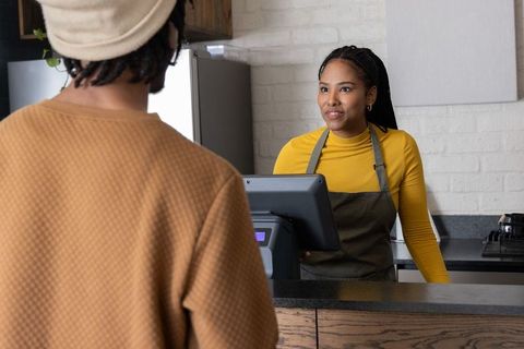 African american barista serving customer at cafe counter using point of sale register