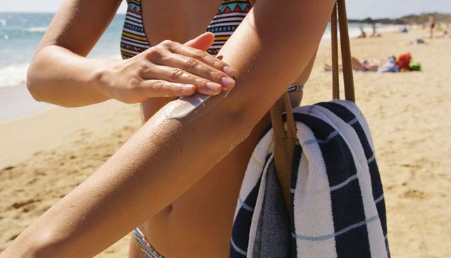 Applying sunscreen on forearm at sunny beach with striped towel and patterned bikini