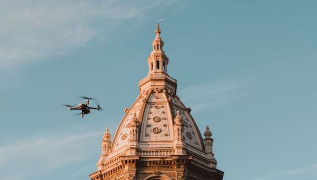 Quadcopter drone hovering by ornate historic dome and cupola at golden hour, architectural detail