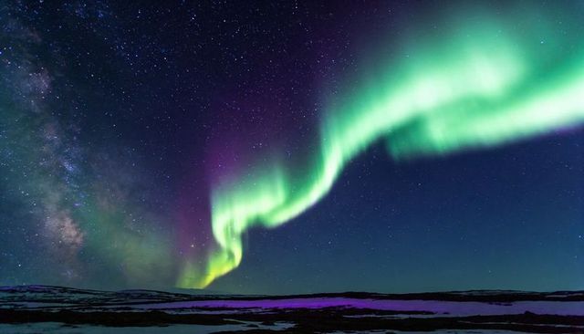 Dancing auroral ribbon sweeping over remote tundra with milky way and starfield