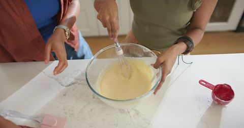 Diverse friends whisking cake batter on white marble countertop, casual home baking moment
