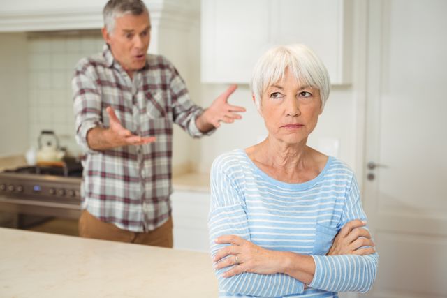 Illustrates a tense moment between an older couple experiencing a disagreement in a domestic kitchen setting. Suitable for articles on relationship challenges, senior living, family dynamics, and emotional health in older adults.