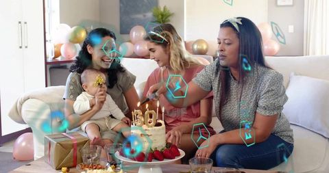 Three women and baby celebrating 30th birthday cake at home party with balloons and gifts