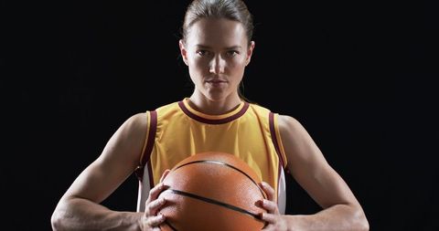 Focused Female Athlete Holding Basketball in Gym